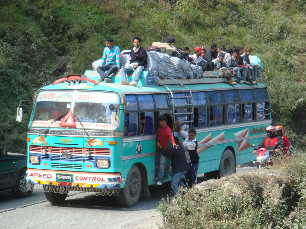 Überfüllter Bus auf einer Bergstraße in Nepal mit Passagieren auf dem Dach während einer typischen Himalaya-Busfahrt.