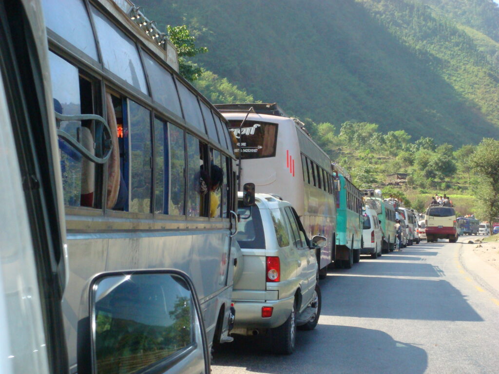 Überfüllter Bus auf einer kurvenreichen Bergstraße in Nepal mit Passagieren auf dem Dach während einer typischen Himalaya-Busfahrt.